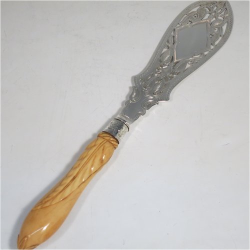 An Antique Victorian sterling silver and ivory-handled fish server slice, having a hand-cut ivory handle with leaf decoration, a hand-pierced symmetrical blade with floral decoration and an engraved scene of a fisherman on one side, together with a silver ferrule between the blade and handle. Made by George Unite of Birmingham in 1872. The length of this fine hand-made antique silver fish serving slice is 31 cms (12.25 inches).
