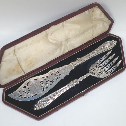 A very pretty Antique Victorian Sterling Silver pair of fish serving knife and fork set, having handles in a double-struck floral pattern with reeded sides, and hand-pierced blade and tines with hand-engraved dolphins, scroll, and floral decoration, all in their original dark blue velvet and cream satin lined presentation box. Made by Martin Hall and Co., of Sheffield in 1859. The dimensions of this fine hand-made antique silver fish serving set are length of knife 33 cms (13 inches), length of fork 25.5 cms (10 inches), and they weigh a total of approx. 300g (9.7 troy ounces).  