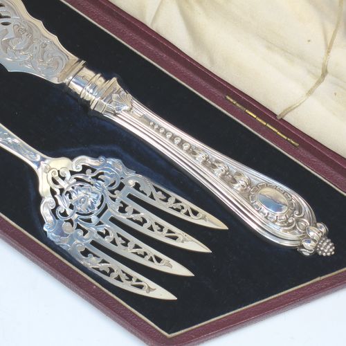 A very pretty Antique Victorian Sterling Silver pair of fish serving knife and fork set, having handles in a double-struck floral pattern with reeded sides, and hand-pierced blade and tines with hand-engraved dolphins, scroll, and floral decoration, all in their original dark blue velvet and cream satin lined presentation box. Made by Martin Hall and Co., of Sheffield in 1859. The dimensions of this fine hand-made antique silver fish serving set are length of knife 33 cms (13 inches), length of fork 25.5 cms (10 inches), and they weigh a total of approx. 300g (9.7 troy ounces).  
