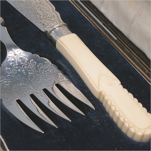 An Antique Victorian Sterling Silver fish serving knife and fork set, having hand-carved bone or ivory handles, with hand-engraved blade and tines with floral decoration, all in their original satin and blue velvet-lined presentation box. Made by James Deakin & Sons of Sheffield in 1887. The dimensions of this fine hand-made antique silver fish serving set are length of knife 31 cms (12.25 inches), and length of fork 24 cms (9.5 inches). Please note that the cream coloured satin upper lining to the lid is slightly damaged.