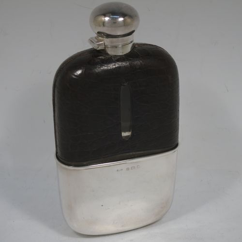 A large and handsome Antique Victorian Sterling Silver and glass whisky flask, with crocodile leather skin mount, and a sight level both sides, having a bayonet fit lid and a pull-off cup with gold-gilt interior. Made in Birmingham in 1900. The dimensions of this fine hand-made antique silver and glass whisky flask are length 18 cms (7 inches), width 9.5 cms (3.75 inches), and depth 4 cms (1.5 inches). Please note slight damage to crocodile skin cover on one side.  