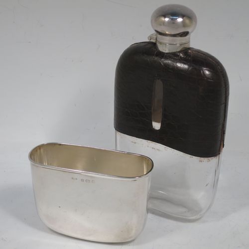 A large and handsome Antique Victorian Sterling Silver and glass whisky flask, with crocodile leather skin mount, and a sight level both sides, having a bayonet fit lid and a pull-off cup with gold-gilt interior. Made in Birmingham in 1900. The dimensions of this fine hand-made antique silver and glass whisky flask are length 18 cms (7 inches), width 9.5 cms (3.75 inches), and depth 4 cms (1.5 inches). Please note slight damage to crocodile skin cover on one side.