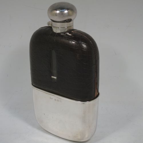 A large and handsome Antique Victorian Sterling Silver and glass whisky flask, with crocodile leather skin mount, and a sight level both sides, having a bayonet fit lid and a pull-off cup with gold-gilt interior. Made in Birmingham in 1900. The dimensions of this fine hand-made antique silver and glass whisky flask are length 18 cms (7 inches), width 9.5 cms (3.75 inches), and depth 4 cms (1.5 inches). Please note slight damage to crocodile skin cover on one side.