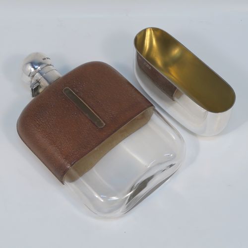 A large and handsome Antique Sterling Silver and glass whisky flask, with leather skin mount, and a sight level both sides, having a bayonet fit lid and a pull-off cup with gold-gilt interior. This elegant silver and glass hip flask was made by James Dixon and Sons of Sheffield in 1924. The dimensions of this fine hand-made silver and glass whisky flask are length 18 cms (7 inches), width 11 cms (4.3 inches), and depth 4 cms (1.5 inches).