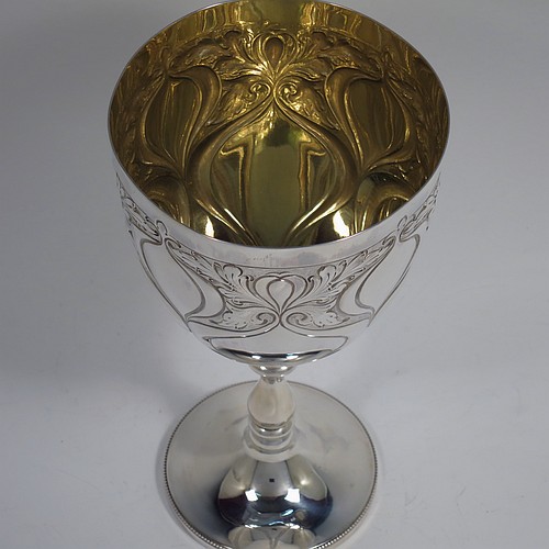 A large Antique Edwardian Sterling Silver Art Nouveau style goblet, having a round tapering body with hand-chased anthemion leaf work and plain tear-drop shaped cartouches, sitting on a pedestal foot with a bead border, and with a gold-gilt interior. Made by the Cooper Brothers of Sheffield in 1904. The dimensions of this fine hand-made antique silver Art Nouveau goblet are height 20 cms (8 inches), diameter at lip 10 cms (4 inches), and it weighs approx. 285g (9.2 troy ounces).