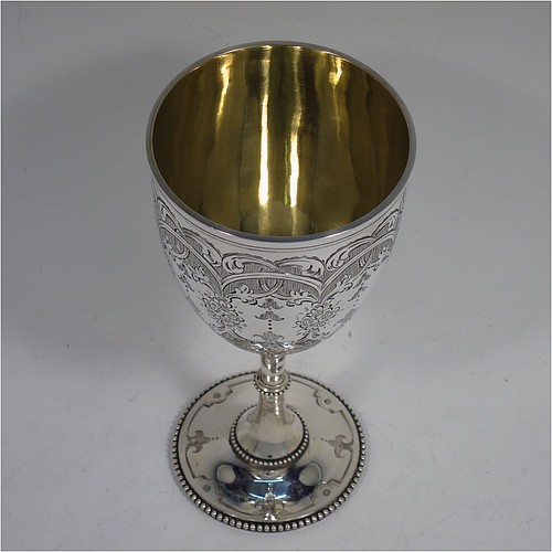 A very pretty Antique Victorian Sterling Silver goblet, having a round bellied body with hand-engraved floral and scroll decoration, with a vacant cartouche on one side, a gold-gilt interior, and sitting on a pedestal foot with hand-engraved decoration and applied bead-edged borders. Made by Henry Wilkinson of London in 1868. The dimensions of this fine hand-made antique silver goblet are height 16.5 cms (6.5 inches), diameter at lip 7.5 cms (3 inches), and it weighs approx. 148g (4.8 troy ounces).