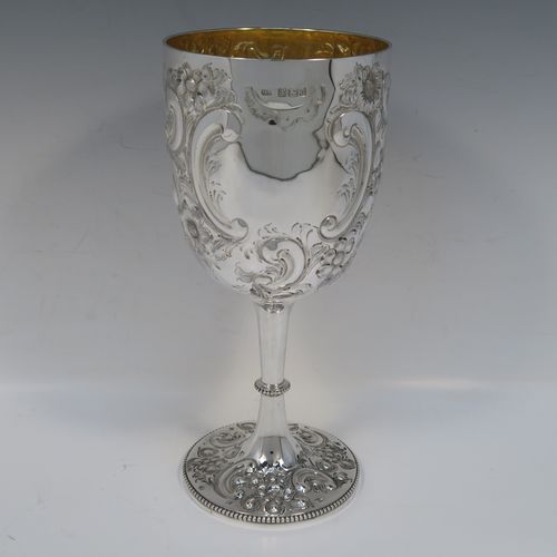 A large and beautiful Antique Victorian sterling silver goblet, having a round body with tapering sides and a gold-gilt interior, all hand-chased with floral and scroll decoration surrounding two vacant cartouches, and sitting on a pedestal foot with matching decoration and applied bead-edged borders. This large and impressive antique silver goblet was made by the Atkin Brothers of Sheffield in 1893. The dimensions of this fine hand-made silver goblet are height 25.5 cms (10 inches), diameter at lip 11.5 cms (4.5 inches), and it weighs approx. 472g (15.2 troy ounces).   