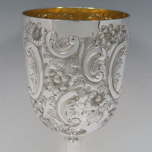 A large and beautiful Antique Victorian sterling silver goblet, having a round body with tapering sides and a gold-gilt interior, all hand-chased with floral and scroll decoration surrounding two vacant cartouches, and sitting on a pedestal foot with matching decoration and applied bead-edged borders. This large and impressive antique silver goblet was made by the Atkin Brothers of Sheffield in 1893. The dimensions of this fine hand-made silver goblet are height 25.5 cms (10 inches), diameter at lip 11.5 cms (4.5 inches), and it weighs approx. 472g (15.2 troy ounces).   