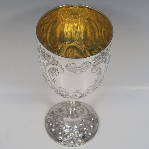 A large and beautiful Antique Victorian sterling silver goblet, having a round body with tapering sides and a gold-gilt interior, all hand-chased with floral and scroll decoration surrounding two vacant cartouches, and sitting on a pedestal foot with matching decoration and applied bead-edged borders. This large and impressive antique silver goblet was made by the Atkin Brothers of Sheffield in 1893. The dimensions of this fine hand-made silver goblet are height 25.5 cms (10 inches), diameter at lip 11.5 cms (4.5 inches), and it weighs approx. 472g (15.2 troy ounces).   