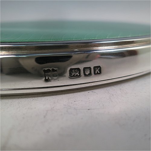 A Sterling Silver Art Deco style hand-mirror, having an oval body and a square cross-section handle, with green enamelled sun-burst style decoration, and an original bevelled mirror. Made by Robert Comyns of London in 1945. The dimensions of this fine hand-made Art Deco silver and green enamelled hand mirror are length 25.5 cms (10 inches), and width 11 cms (4.3 inches).