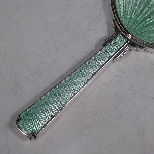 A Sterling Silver Art Deco style hand-mirror, having an oval body and a square cross-section handle, with green enamelled sun-burst style decoration, and an original bevelled mirror. Made by Robert Comyns of London in 1945. The dimensions of this fine hand-made Art Deco silver and green enamelled hand mirror are length 25.5 cms (10 inches), and width 11 cms (4.3 inches).
