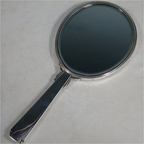 A Sterling Silver Art Deco style hand-mirror, having an oval body and a square cross-section handle, with green enamelled sun-burst style decoration, and an original bevelled mirror. Made by Robert Comyns of London in 1945. The dimensions of this fine hand-made Art Deco silver and green enamelled hand mirror are length 25.5 cms (10 inches), and width 11 cms (4.3 inches).