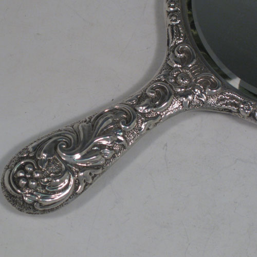 Antique Edwardian sterling silver hand-mirror, having a round body with hand-chased floral decoration, a central vacant cartouche, and a round bevelled mirror. Made by Nathan and Hayes of Chester in 1902. The dimensions of this fine hand-made silver hand mirror are length 28 cms (11 inches), and width 16.5 cms (6.5 inches).
