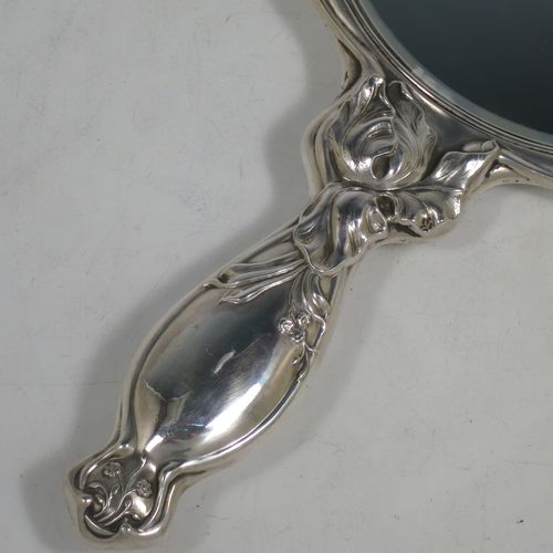 A very pretty Art Nouveau Antique Edwardian Sterling Silver hand-mirror, having a round body with hand-chased Iris floral decoration, and a round bevelled mirror with a lobed border. Made by William Aitken of Birmingham in 1909. The dimensions of this fine hand-made antique Art Nouveau silver hand mirror are length 28 cms (11 inches), and diameter 16 cms (6.25 inches).