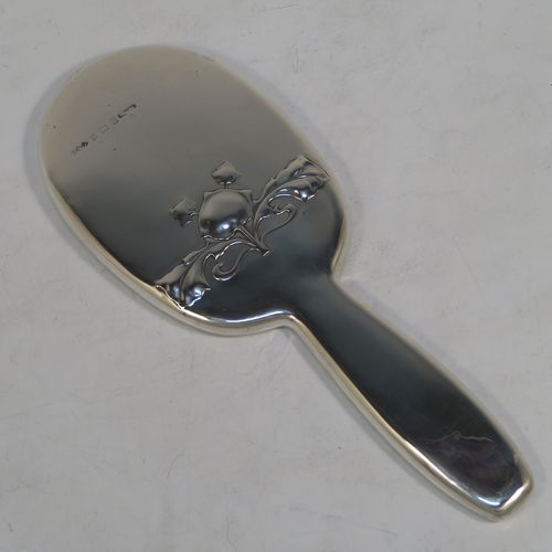 A very pretty and rare Antique Edwardian Arts and Crafts style Sterling Silver hand-mirror, having a plain rounded rectangular body with a hand-chased floral style motif in the Cymric pattern, an original bevelled mirror, and a plain handle. Designed and made by the famous Liberty and Company of Birmingham in 1902. The dimensions of this fine hand-made Arts and Crafts style silver hand mirror are length 24 cms (9.5 inches), and width 9 cms (3.5 inches).   
