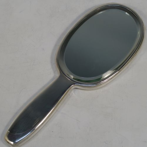 A very pretty and rare Antique Edwardian Arts and Crafts style Sterling Silver hand-mirror, having a plain rounded rectangular body with a hand-chased floral style motif in the Cymric pattern, an original bevelled mirror, and a plain handle. Designed and made by the famous Liberty and Company of Birmingham in 1902. The dimensions of this fine hand-made Arts and Crafts style silver hand mirror are length 24 cms (9.5 inches), and width 9 cms (3.5 inches).