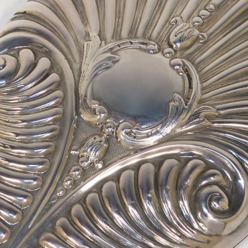 A very elegant Antique Edwardian Sterling Silver hand-mirror, having an oval body with hand-chased fluting and scroll-work surrounding a central vacant cartouche, and an oval bevelled mirror with a plain border. This beautiful silver hand mirror was made by Edward Bennet of London in 1904. The dimensions of this fine hand-made antique silver hand mirror are length 27 cms (10.6 inches), and width of main body 11.5 cms (4.5 inches).