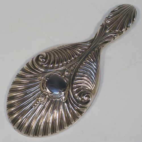 A very elegant Antique Edwardian Sterling Silver hand-mirror, having an oval body with hand-chased fluting and scroll-work surrounding a central vacant cartouche, and an oval bevelled mirror with a plain border. This beautiful silver hand mirror was made by Edward Bennet of London in 1904. The dimensions of this fine hand-made antique silver hand mirror are length 27 cms (10.6 inches), and width of main body 11.5 cms (4.5 inches).