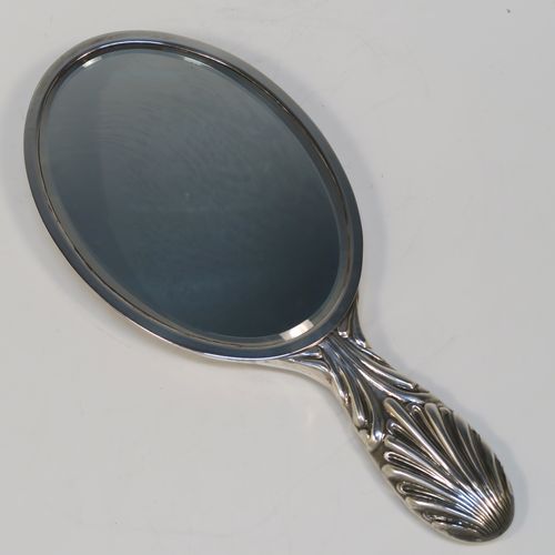 A very elegant Antique Edwardian Sterling Silver hand-mirror, having an oval body with hand-chased fluting and scroll-work surrounding a central vacant cartouche, and an oval bevelled mirror with a plain border. This beautiful silver hand mirror was made by Edward Bennet of London in 1904. The dimensions of this fine hand-made antique silver hand mirror are length 27 cms (10.6 inches), and width of main body 11.5 cms (4.5 inches).