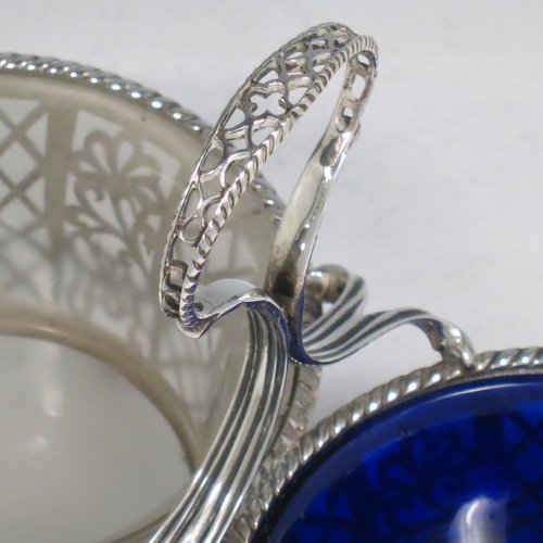 An Antique Edwardian Sterling Silver preserve, jam and honey pot holder, having a blue and frosted glass pot, sitting in a hand-pierced frame with floral and geometric decoration, with applied gadroon borders, a reeded and pierced loop handle, and all sitting on four cast floral feet. Made by Mappin and Webb of London in 1907. The dimensions of this fine hand-made antique silver and glass preserve holder are length 21 cms (8.25 inches), width 11 cms (4.25 inches), height 17.5 cms (7 inches), and it weighs approx. 243g (7.8 troy ounces).
