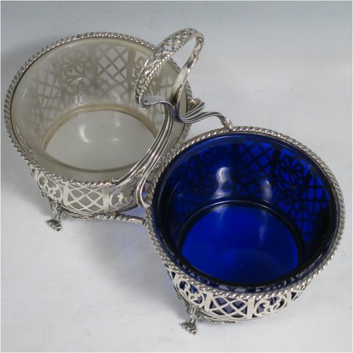 An Antique Edwardian Sterling Silver preserve, jam and honey pot holder, having a blue and frosted glass pot, sitting in a hand-pierced frame with floral and geometric decoration, with applied gadroon borders, a reeded and pierced loop handle, and all sitting on four cast floral feet. Made by Mappin and Webb of London in 1907. The dimensions of this fine hand-made antique silver and glass preserve holder are length 21 cms (8.25 inches), width 11 cms (4.25 inches), height 17.5 cms (7 inches), and it weighs approx. 243g (7.8 troy ounces).