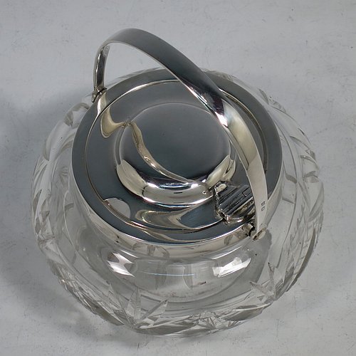 A Sterling Silver and crystal honey or jam jar, having a round bellied body with hand-cut geometrical design and a star-cut base, a plain round mount, with a mechanical swing-handled hinged and domed lid. Made by Hukin & Heath of Birminghamn in 1928. The dimensions of this fine hand-made silver and glass conserve jar are height (inc. handle) 12.5 cms (5 inches), and diameter 11 cms (4.3 inches).