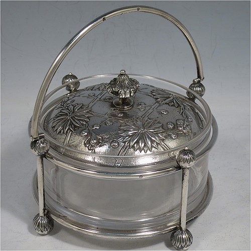 An Antique Victorian Scottish Sterling Silver and crystal Aesthetic style honey, jam, or butter dish, having a round straight-sided clear body sitting in a wire-work frame, with a swing-handle, and a lift-off lid with hand-chased Chrysanthemums, and all sitting on four ball feet. Made by Hamilton & Inches of Edinburgh in 1877/79. The dimensions of this fine hand-made antique silver and glass butter dish or conserve jar are height (inc. handle) 14 cms (5.5 inches), diameter 13 cms (5 inches), and it weighs approx. 327g (10.5 troy ounces).    