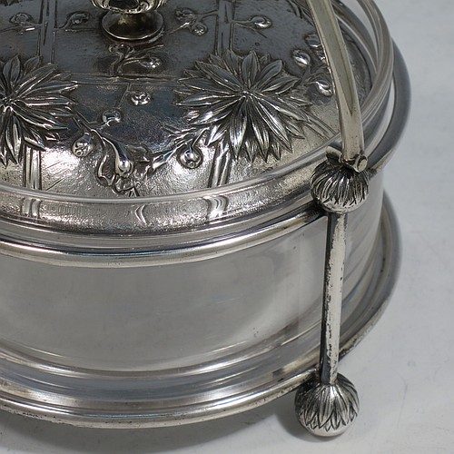 An Antique Victorian Scottish Sterling Silver and crystal Aesthetic style honey, jam, or butter dish, having a round straight-sided clear body sitting in a wire-work frame, with a swing-handle, and a lift-off lid with hand-chased Chrysanthemums, and all sitting on four ball feet. Made by Hamilton & Inches of Edinburgh in 1877/79. The dimensions of this fine hand-made antique silver and glass butter dish or conserve jar are height (inc. handle) 14 cms (5.5 inches), diameter 13 cms (5 inches), and it weighs approx. 327g (10.5 troy ounces).