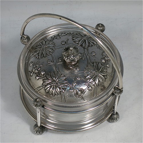 An Antique Victorian Scottish Sterling Silver and crystal Aesthetic style honey, jam, or butter dish, having a round straight-sided clear body sitting in a wire-work frame, with a swing-handle, and a lift-off lid with hand-chased Chrysanthemums, and all sitting on four ball feet. Made by Hamilton & Inches of Edinburgh in 1877/79. The dimensions of this fine hand-made antique silver and glass butter dish or conserve jar are height (inc. handle) 14 cms (5.5 inches), diameter 13 cms (5 inches), and it weighs approx. 327g (10.5 troy ounces).