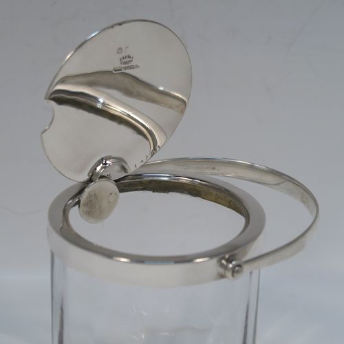 A very elegant Art Deco Sterling Silver and crystal honey or jam jar, having a plain cylindrical and panelled body with star-cut base, a plain round mount, and a plain mechanical swing-handled hinged lid with cut-out for a honey or jam spoon (not included). This handsome silver honey or jam jar was made by Asprey of Birmingham in 1935. The dimensions of this fine hand-made silver and crystal conserve jar are height (inc. handle) 15 cms (6 inches), and diameter 8 cms (3 inches).