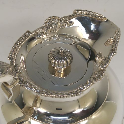 A very handsome Antique Edwardian Sterling Silver hot water or milk pot, having a round bellied body, with hand-chased half-fluted decoration and an applied gadroon and shell top border, with an insulated silver scroll handle and an invisibly hinged lid with a cast fluted finial, and all sitting on a pedestal foot. This beautiful antique silver hot milk or water pot was made by Sebastian Garrard of London in 1910. The dimensions of this fine hand-made antique silver serving pot are height 20 cms (8 inches), length 18.5 cms (7.25 inches), and it weighs approx. 758g (24.5 troy ounces).   