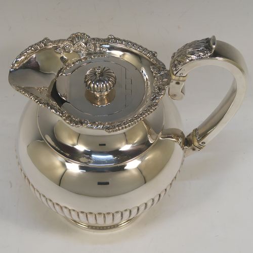 A very handsome Antique Edwardian Sterling Silver hot water or milk pot, having a round bellied body, with hand-chased half-fluted decoration and an applied gadroon and shell top border, with an insulated silver scroll handle and an invisibly hinged lid with a cast fluted finial, and all sitting on a pedestal foot. This beautiful antique silver hot milk or water pot was made by Sebastian Garrard of London in 1910. The dimensions of this fine hand-made antique silver serving pot are height 20 cms (8 inches), length 18.5 cms (7.25 inches), and it weighs approx. 758g (24.5 troy ounces).   