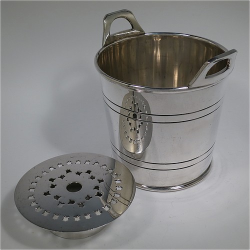 An Antique Edwardian silver plated ice bucket, having a plain round body with tapering straight sides and hand-chased reeded decoration, an internal removable dry ice drainer, with two top cast side handles, and all sitting on a flat base. Made by Collins of London in ca. 1910. The dimensions of this fine hand-made antique silver-plated ice bucket are height 15.5 cms (6 inches), and diameter at lip 14 cms (5.5 inches).   