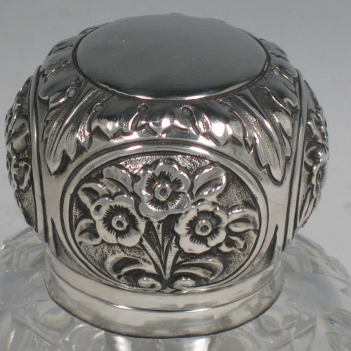 Antique Victorian Art Nouveau sterling silver inkstand, having a hand-chased hinged lid with floral decoration, a glass insert for a smaller amount of ink, and a heavy hand-cut round crystal body that can hold a large amount of ink, with a star cut base. Made by Mappin and Webb of London in 1899. Height 12.5 cms (5 inches), diameter 10 cms (4 inches).