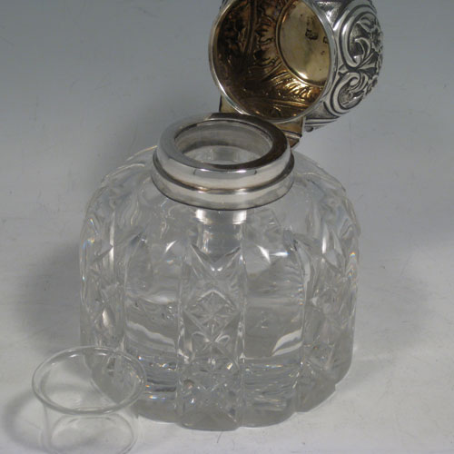 Antique Victorian Art Nouveau sterling silver inkstand, having a hand-chased hinged lid with floral decoration, a glass insert for a smaller amount of ink, and a heavy hand-cut round crystal body that can hold a large amount of ink, with a star cut base. Made by Mappin and Webb of London in 1899. Height 12.5 cms (5 inches), diameter 10 cms (4 inches).