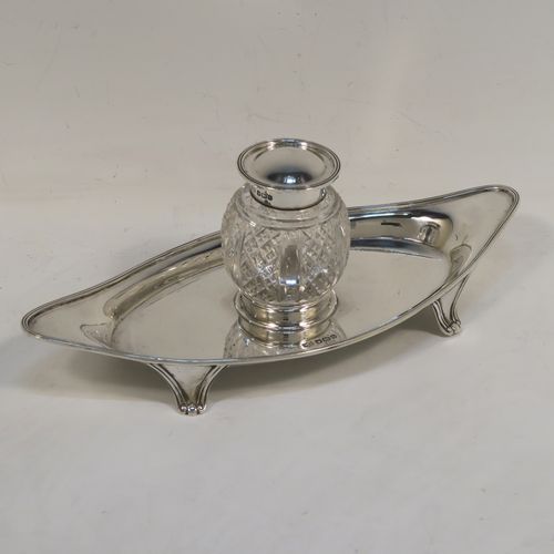 An elegant Antique Sterling Silver single bottle inkstand, with a plain oval boat-shaped body, having an applied reeded border, a single removable cut-crystal ink bottle with hinged lid, and all sitting on four cast flanged feet. This pretty antique silver inkstand was made by Mappin and Webb of Sheffield in 1911. The dimensions of this fine hand-made antique sterling silver inkstand are length 21 cms (8.25 inches), width 9.5 cms (3.75 inches), and it weighs approx. 150g (4.8 troy ounces).  