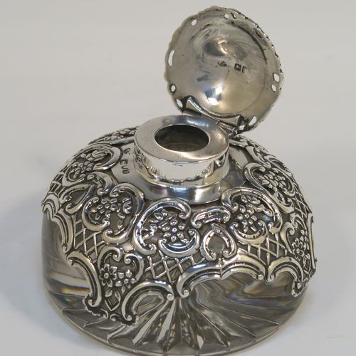 A beautiful Antique Victorian Sterling Silver and hand-cut crystal inkstand, having a round body with a hand-pierced and hand-chased overlay with floral and scroll decoration, a hinged lid with an applied floral border, and sitting on a hand-cut star flat base. This very pretty silver and crystal inkstand was made by William Comyns of London in 1897. The dimensions of this fine hand-made antique silver and crystal inkstand are height 6 cms (2.3 inches), and diameter 9 cms (3.5 inches).   