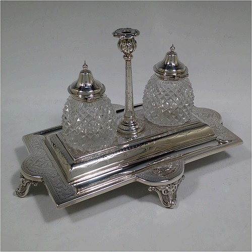 A very pretty and large Antique Victorian Sterling Silver double bottle inkstand, having a rectangular body with a hand-engraved floral and scroll decoration, two pineapple shaped hand-cut crystal removable ink bottles with round domed hinged lids, together with a central taper-stick candle holder, and all sitting on four cast shell and foliate feet. Made by Samuel, Robert, and Charles Belk of Sheffield in 1867. The dimensions of this fine hand-made antique silver double inkstand are length 30.5 cms (12 inches), width 21 cms (8.25 inches), height 18.5 cms (7.25 inches), and it weighs approx. 540g (17.4 troy ounces).   