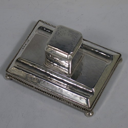 A very pretty Sterling Silver inkstand, in an Arts and Crafts hand-hammered or plenished style, having a single inkwell with a hinged lid and removable glass liner, sitting on a stand with two pen-wells, applied rope-twist borders, and four ball cushion feet. Made in London in 1930. The dimensions of this fine hand-made silver inkstand are height 6.5 cms (2.5 inches), length 11 cms (4.25 inches), width 8 cms (3.25 inches), and it weighs approx. 150g (4.8 troy ounces).    