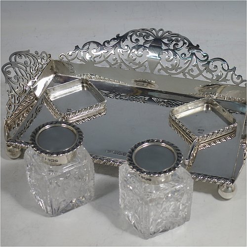 A very pretty Antique Edwardian Sterling Silver galleried double inkstand, having a rectangular body with three hand-pierced scroll-work gallery sides, an applied gadroon front border, two square hand-cut crystal removable ink bottles with round hinged lids, together with two applied pen-rest scrolls, all sitting on four ball feet. Made by George Wish of Sheffield in 1905. The dimensions of this fine hand-made antique silver double inkstand are length 22 cms (8.75 inches), width 14 cms (5.5 inches), height 5 cms (2 inches), and it weighs approx. 334g (10.8 troy ounces).   