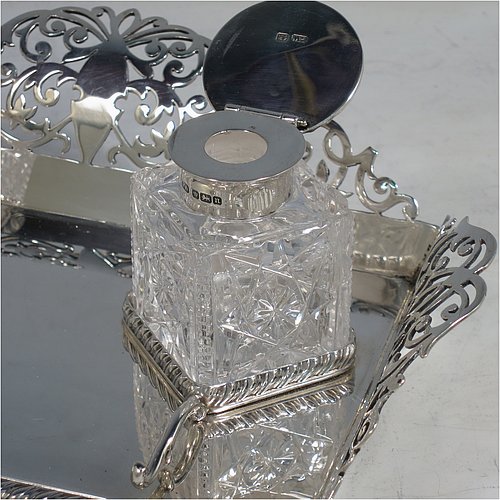 A very pretty Antique Edwardian Sterling Silver galleried double inkstand, having a rectangular body with three hand-pierced scroll-work gallery sides, an applied gadroon front border, two square hand-cut crystal removable ink bottles with round hinged lids, together with two applied pen-rest scrolls, all sitting on four ball feet. Made by George Wish of Sheffield in 1905. The dimensions of this fine hand-made antique silver double inkstand are length 22 cms (8.75 inches), width 14 cms (5.5 inches), height 5 cms (2 inches), and it weighs approx. 334g (10.8 troy ounces).   