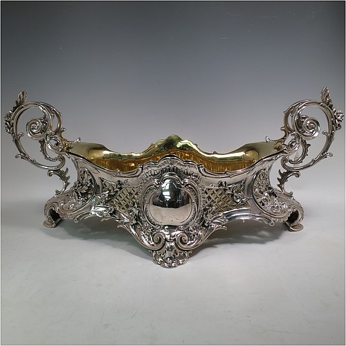 A very impressive and pretty Antique Victorian silver jardiniere, having an oval hand-chased and pierced body with applied floral decoration, two cast scroll-work handles with shell thumb-pieces, sitting on four cast foliate feet, and with an original gold-gilt interior liner. Probably German in origin and made in circa. 1880 in the 800 standard silver. The dimensions of this fine hand-made silver jardinière are Length 67 cms (26.5 inches), width 33 cms (13 inches), height 28 cms (11 inches), and it weighs approx. 4,140g (134 troy ounces).