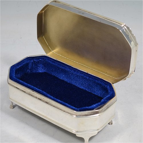 A Sterling Silver Art Deco style jewellery box, having an elongated octagonal body with plain panelled sides, a hinged lid with an applied bright-cut border and engine-turned decoration, a blue velvet-lined and gold-gilt interior, and sitting on four elegant cabriolet legs. Made by Alexander Clarke & Co., of Birmingham in 1931. The dimensions of this fine hand-made silver jewelery box are length 11.5 cms (4.5 inches), width 6.5 cms (2.5 inches), and height 5 cms (2 inches).