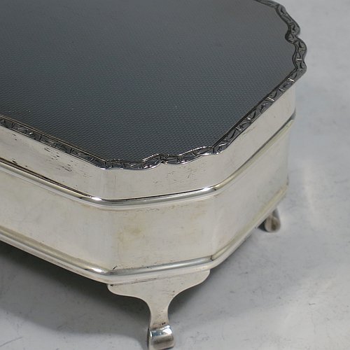 A Sterling Silver Art Deco style jewellery box, having an elongated octagonal body with plain panelled sides, a hinged lid with an applied bright-cut border and engine-turned decoration, a blue velvet-lined and gold-gilt interior, and sitting on four elegant cabriolet legs. Made by Alexander Clarke & Co., of Birmingham in 1931. The dimensions of this fine hand-made silver jewelery box are length 11.5 cms (4.5 inches), width 6.5 cms (2.5 inches), and height 5 cms (2 inches).