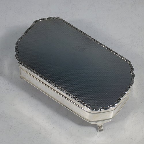 A Sterling Silver Art Deco style jewellery box, having an elongated octagonal body with plain panelled sides, a hinged lid with an applied bright-cut border and engine-turned decoration, a blue velvet-lined and gold-gilt interior, and sitting on four elegant cabriolet legs. Made by Alexander Clarke & Co., of Birmingham in 1931. The dimensions of this fine hand-made silver jewelery box are length 11.5 cms (4.5 inches), width 6.5 cms (2.5 inches), and height 5 cms (2 inches).