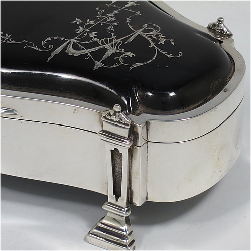 A very pretty and large Antique Sterling Silver and tortoise-shell jewellery box, having an oval shaped body, a tortoise-shell hinged lid with in-laid flowers and ribbon bows, a dark blue velvet-lined interior, and sitting on four cast stepped and columnar style feet. Made by William Comyns of London in 1913. The dimensions of this fine hand-made antique silver and tortoise-shell jewelery box are length 20 cms (8 inches), width 12.5 cms (5 inches), and height 7 cms (2.75 inches).