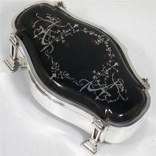 A very pretty and large Antique Sterling Silver and tortoise-shell jewellery box, having an oval shaped body, a tortoise-shell hinged lid with in-laid flowers and ribbon bows, a dark blue velvet-lined interior, and sitting on four cast stepped and columnar style feet. Made by William Comyns of London in 1913. The dimensions of this fine hand-made antique silver and tortoise-shell jewelery box are length 20 cms (8 inches), width 12.5 cms (5 inches), and height 7 cms (2.75 inches).