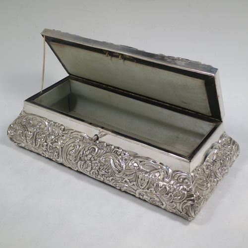 A very pretty Antique Edwardian Sterling Silver large jewellery box, having a rectangular shaped casket style body, with hand-chased floral and scroll decoration, a lockable hinged lid with a vacant central cartouche, a light blue satin-lined interior, all sitting on a flat base. Made by William Comyns of London in 1907. The dimensions of this fine hand-made silver jewellery box are length 27 cms (10.5 inches), width 13 cms (5 inches), and height 9 cms (3.5 inches).