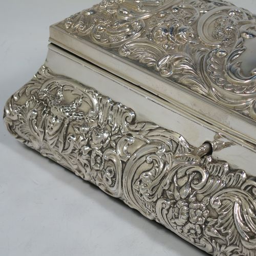 A very pretty Antique Edwardian Sterling Silver large jewellery box, having a rectangular shaped casket style body, with hand-chased floral and scroll decoration, a lockable hinged lid with a vacant central cartouche, a light blue satin-lined interior, all sitting on a flat base. Made by William Comyns of London in 1907. The dimensions of this fine hand-made silver jewellery box are length 27 cms (10.5 inches), width 13 cms (5 inches), and height 9 cms (3.5 inches).