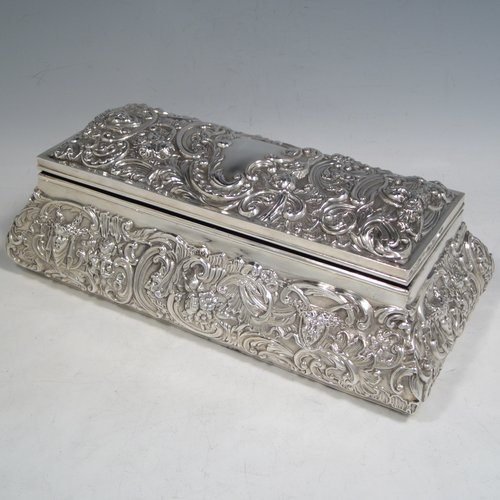 Antique Edwardian sterling silver large jewellery box, having a rectangular shaped casket style body, with hand-chased floral decoration, a hinged lid, a blue velvet and satin-lined interior, all sitting on a flat base. Made by William Comyns of London in 1905. The dimensions of this fine hand-made silver jewellery box are length 27 cms (10.5 inches), width 13 cms (5 inches), and height 9 cms (3.5 inches).